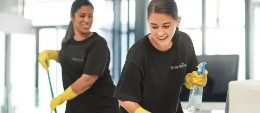 2 Simply Spotless cleaners cheerfully cleaning a commercial office space
