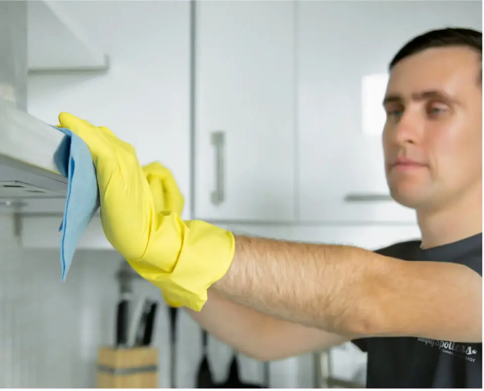 Male Simply Spotless worker cleaning a range hood in a kitchen during an end of lease cleaning service