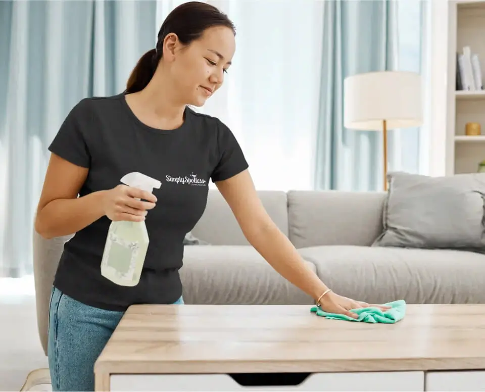 Simply Spotless employee cleaning a coffee table in a living room during a house cleaning service
