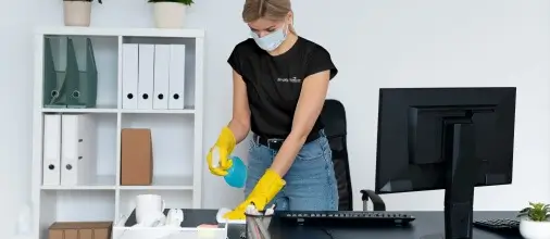Simply Spotless employee cleaning a desk space during an office cleaning service