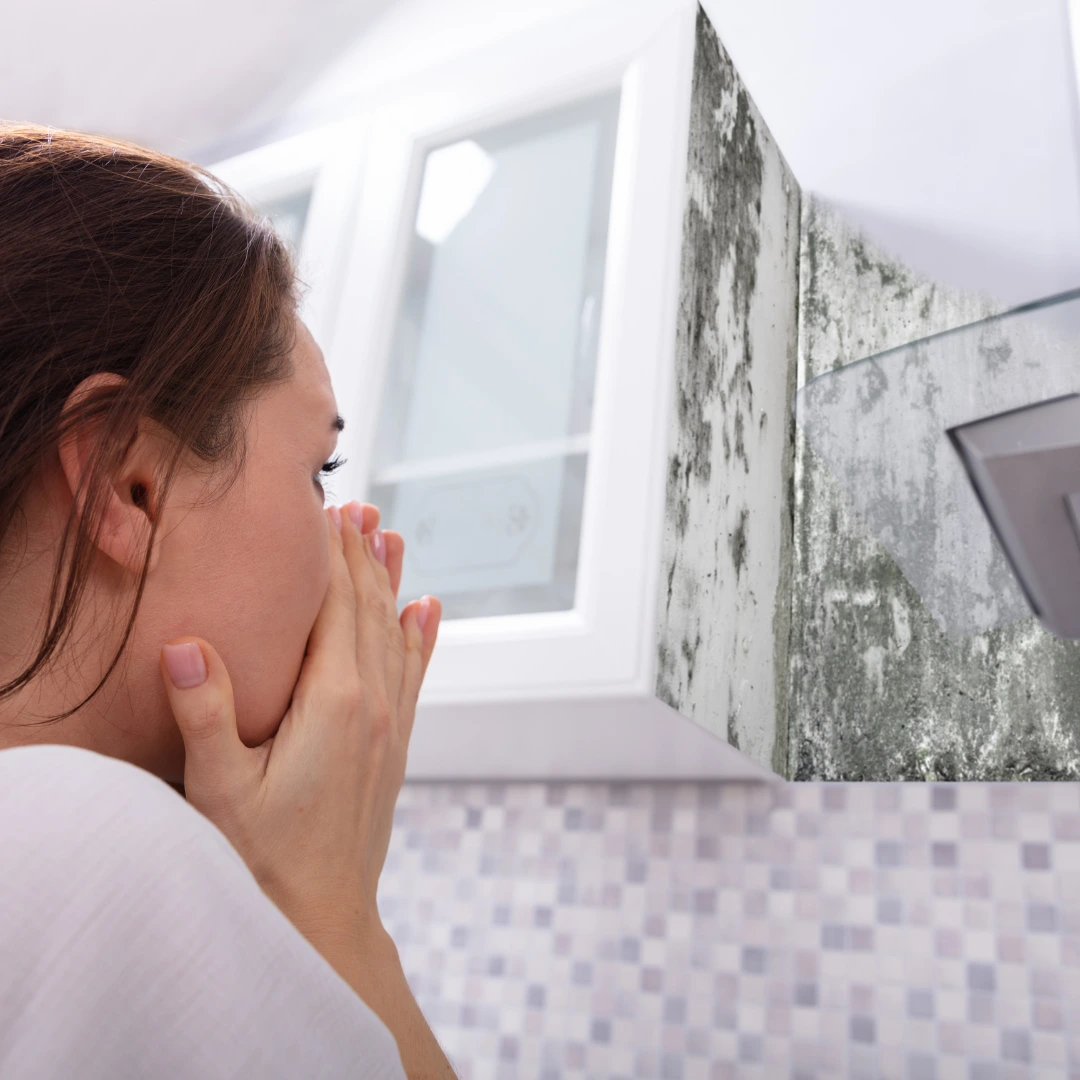 A woman holding her nose at the mould in her bathroom